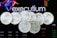 Several silver coins with the inscription 'EXU' are arranged in a pile. In the background, there is an electronic trading platform screen with the word 'executium', some graphs, and trading data.