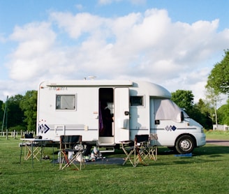 white and brown rv trailer on green grass field under white cloudy sky during daytime