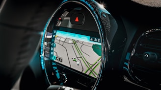 A car interior focusing on the dashboard with a built-in GPS navigation system. The screen displays a map with streets highlighted in green and gray. The dashboard has a modern design with illuminated blue lights outlining the circular screen.