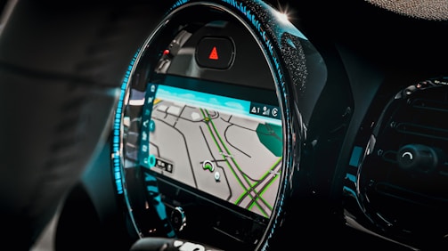 A car interior focusing on the dashboard with a built-in GPS navigation system. The screen displays a map with streets highlighted in green and gray. The dashboard has a modern design with illuminated blue lights outlining the circular screen.