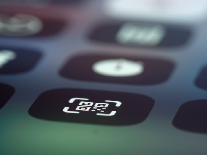 Close-up image of a digital screen displaying app icons, with one prominently featuring a QR code symbol inside a square with rounded corners.