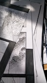 A collection of black and white comic panels featuring detailed illustrations of trees. The scene captures the texture of tree bark and the intricacy of leaves, with strong contrast between light and shadow. A drawing pen lies beside the panels.