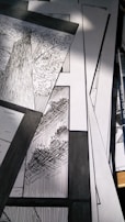 A collection of black and white comic panels featuring detailed illustrations of trees. The scene captures the texture of tree bark and the intricacy of leaves, with strong contrast between light and shadow. A drawing pen lies beside the panels.