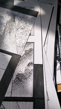A collection of black and white comic panels featuring detailed illustrations of trees. The scene captures the texture of tree bark and the intricacy of leaves, with strong contrast between light and shadow. A drawing pen lies beside the panels.