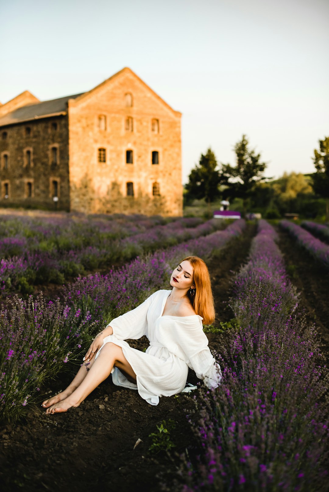 woman in white dress sitting on purple flower field during daytime