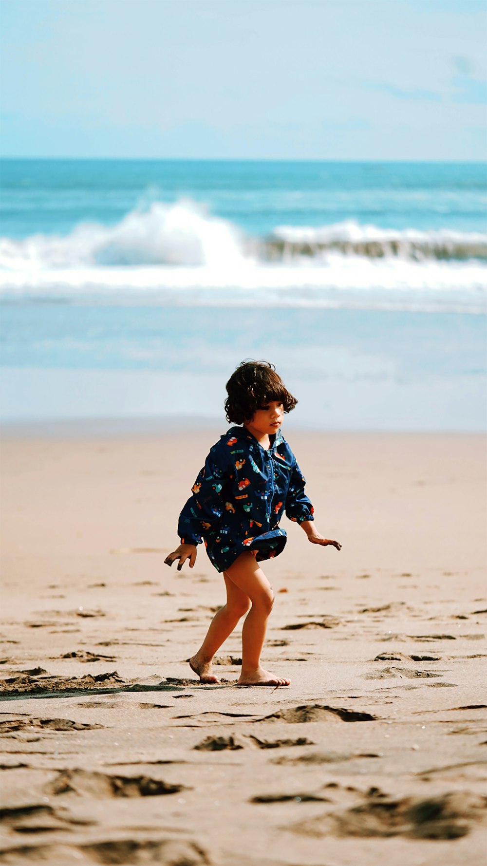 menina no vestido floral azul e branco que anda na praia durante o dia