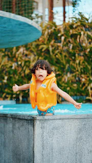 Smiling lifeguard helping a child put on a bright orange flotation vest by the sandy shore.