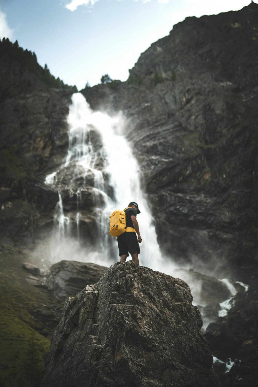 man in orange jacket standing on rock near waterfalls during daytime