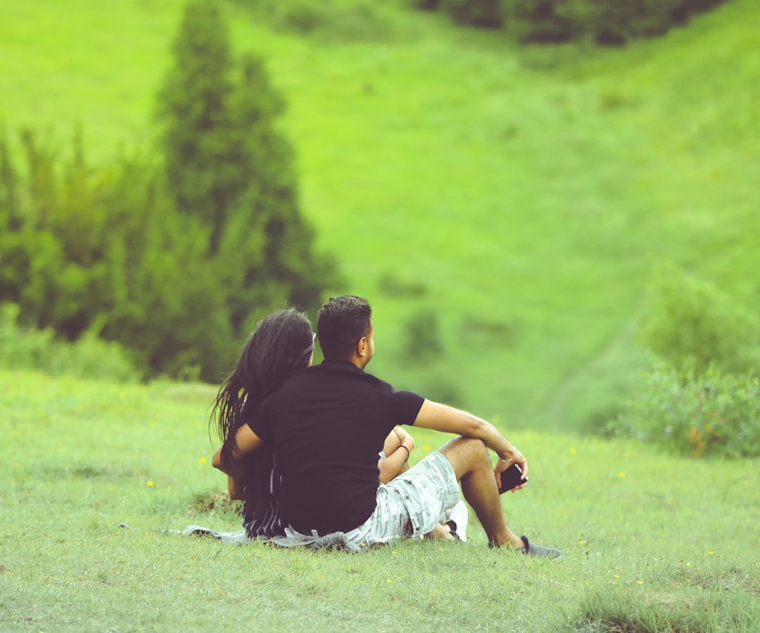 man and woman sitting on green grass field during daytime