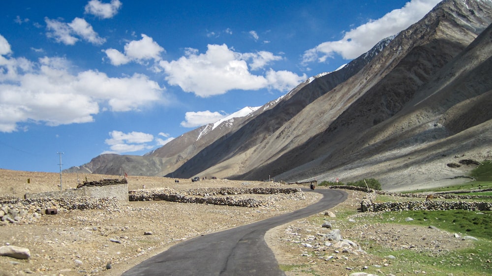 gray concrete road near brown and gray mountains under blue sky during daytime