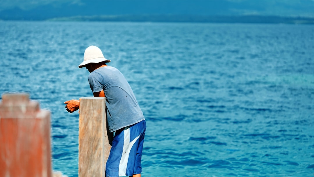 man in grey shirt and blue and white pants standing on brown wooden dock during daytime