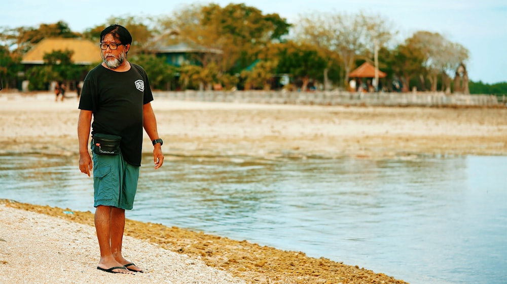homem em camiseta preta do pescoço da tripulação e shorts verdes em pé na areia marrom perto do corpo