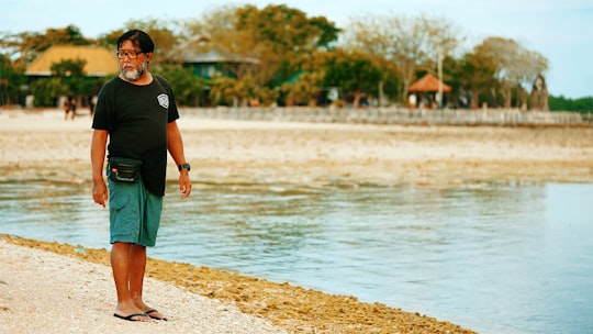 man in black crew neck t-shirt and green shorts standing on brown sand near body in Menjangan Island Indonesia