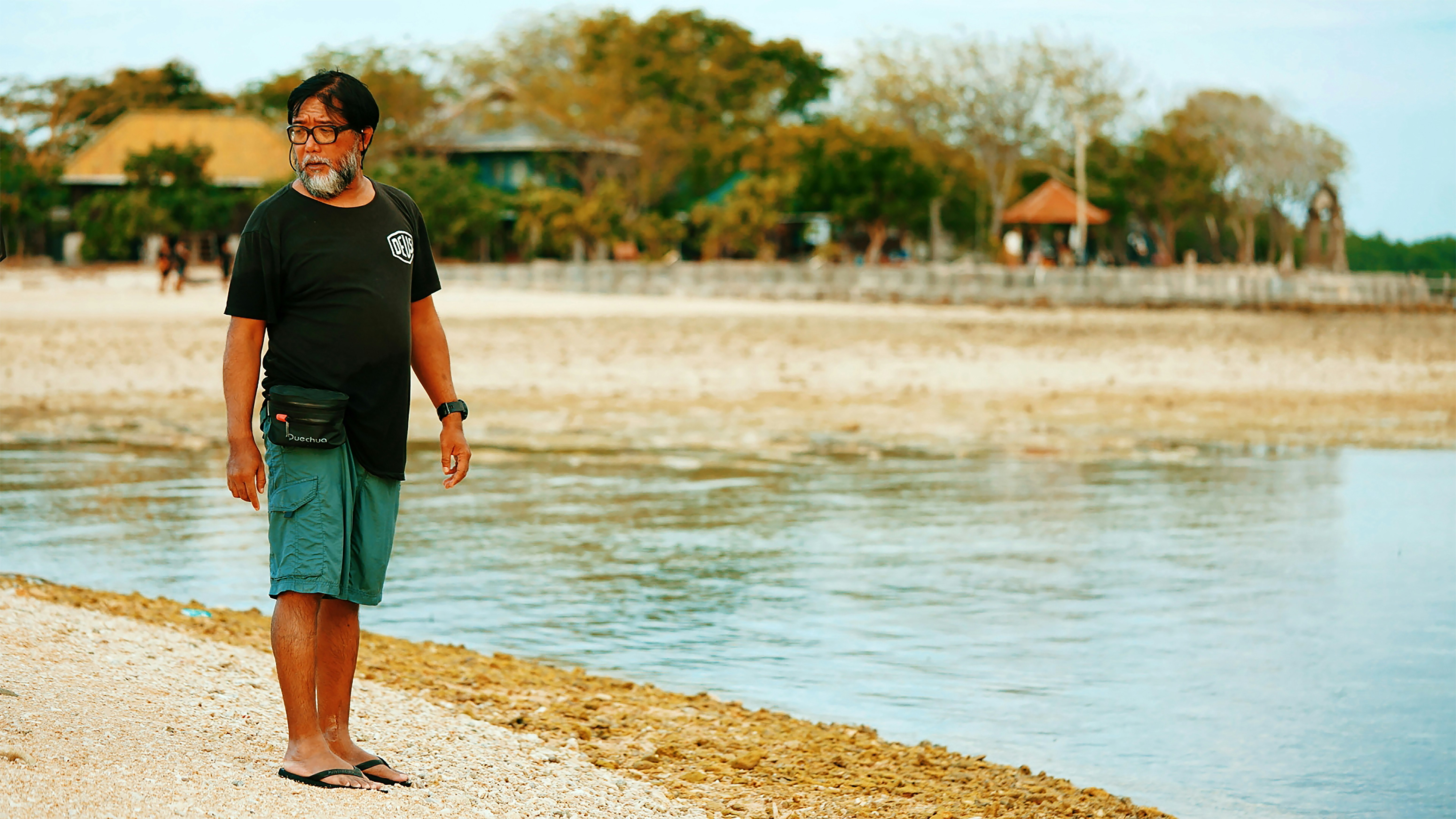 man in black crew neck t-shirt and green shorts standing on brown sand near body