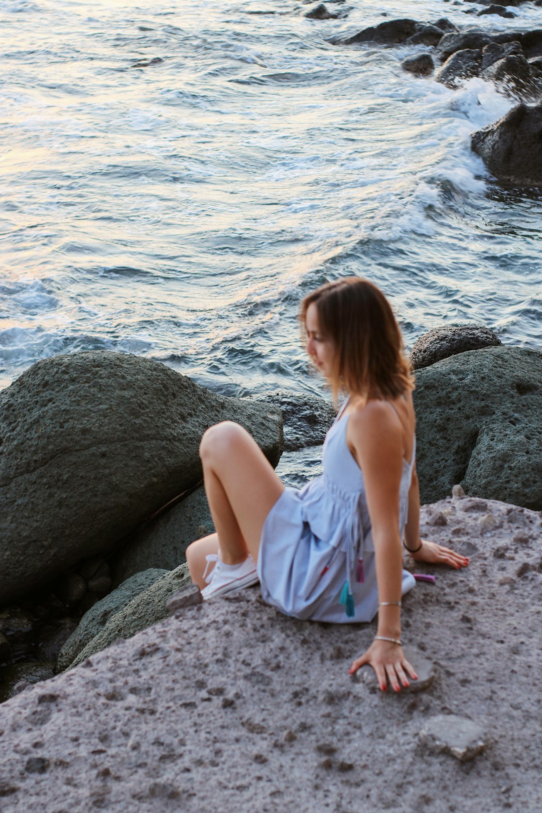 woman in white dress sitting on rock near body of water during daytime