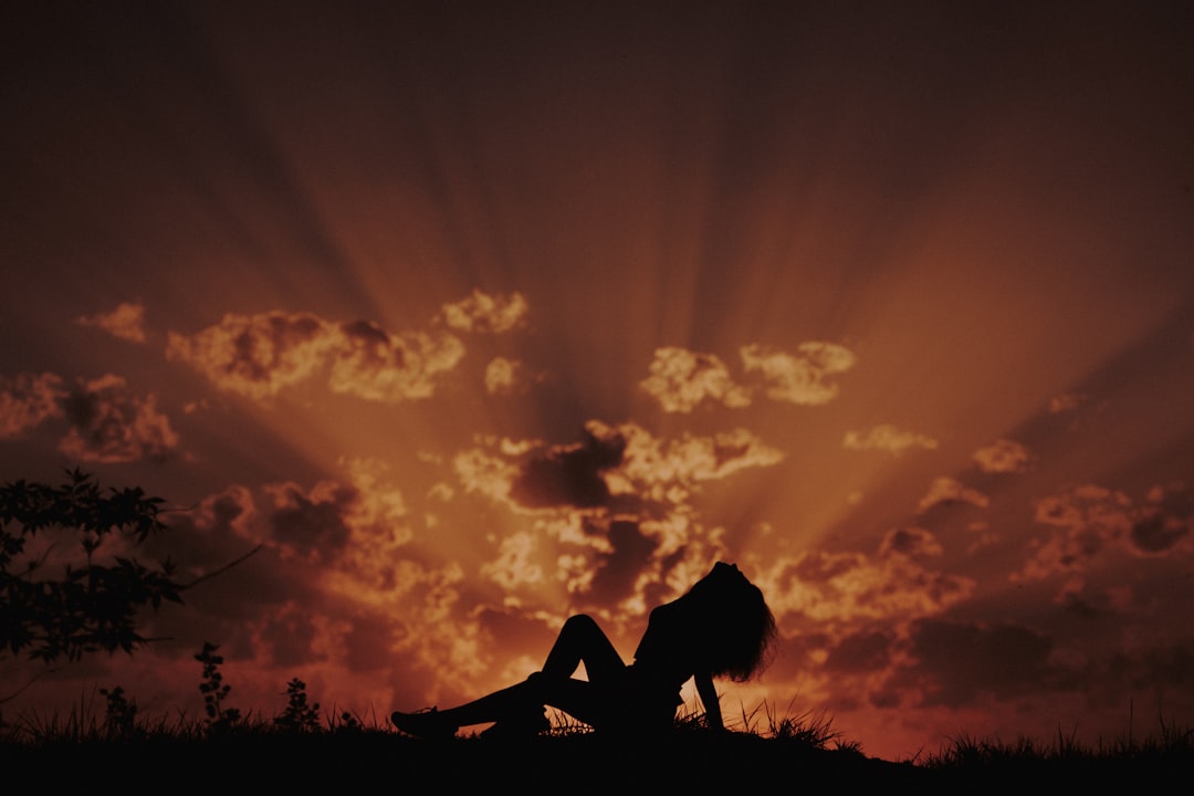 silhouette of woman sitting on grass field during sunset