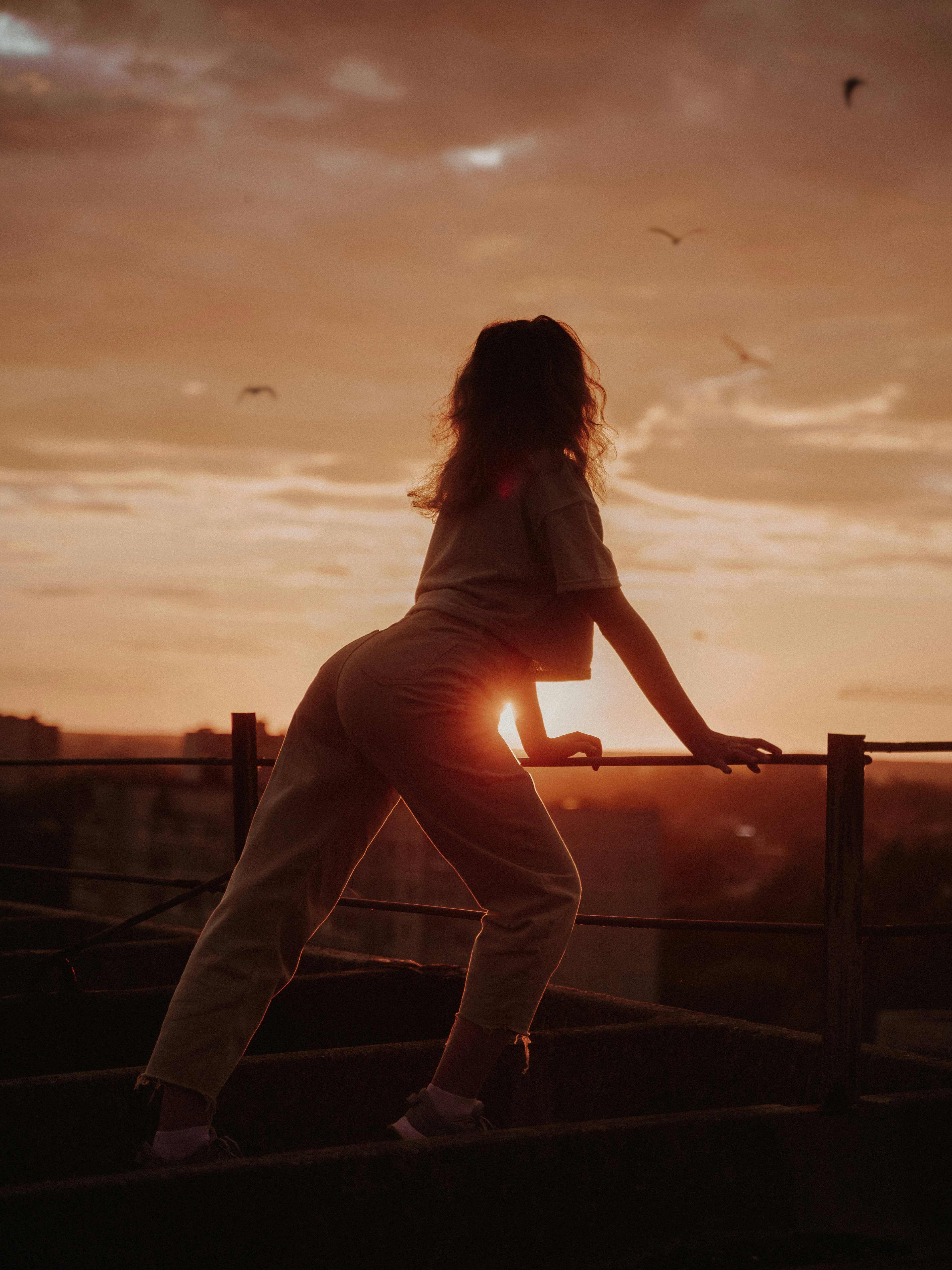 woman in white shirt and pants sitting on railings during sunset