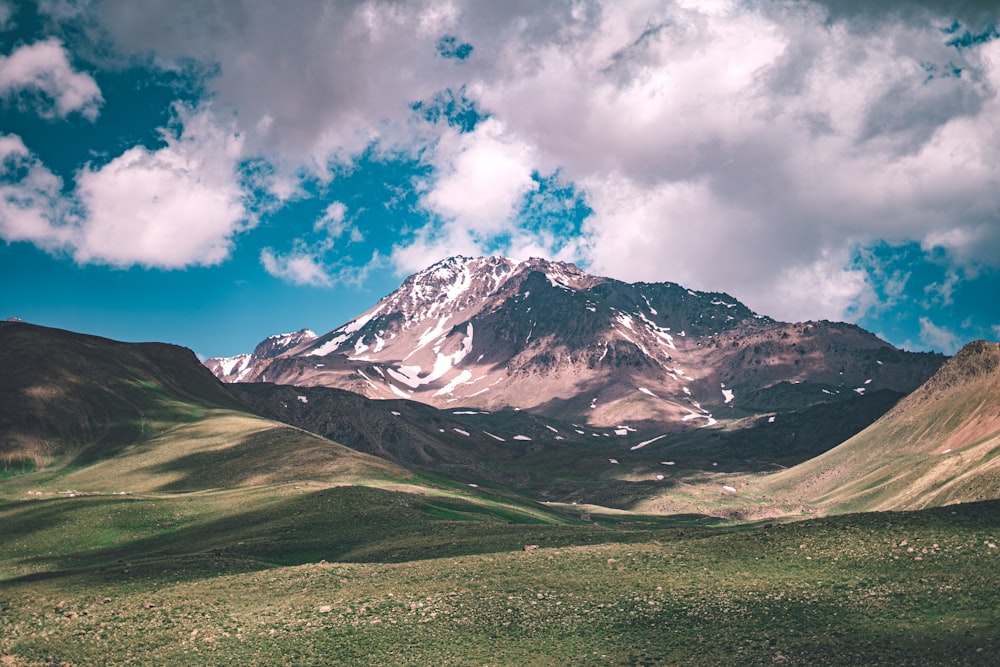 green grass field near snow covered mountain under blue sky and white clouds during daytime