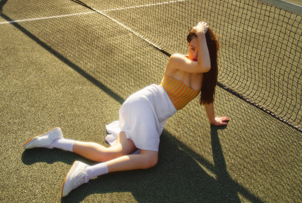 woman in brown tank top and white pants sitting on gray concrete pavement