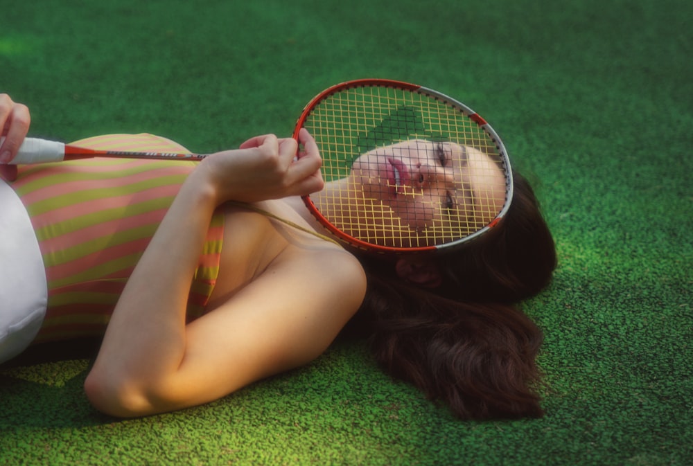 woman lying on green textile holding white and black tennis racket