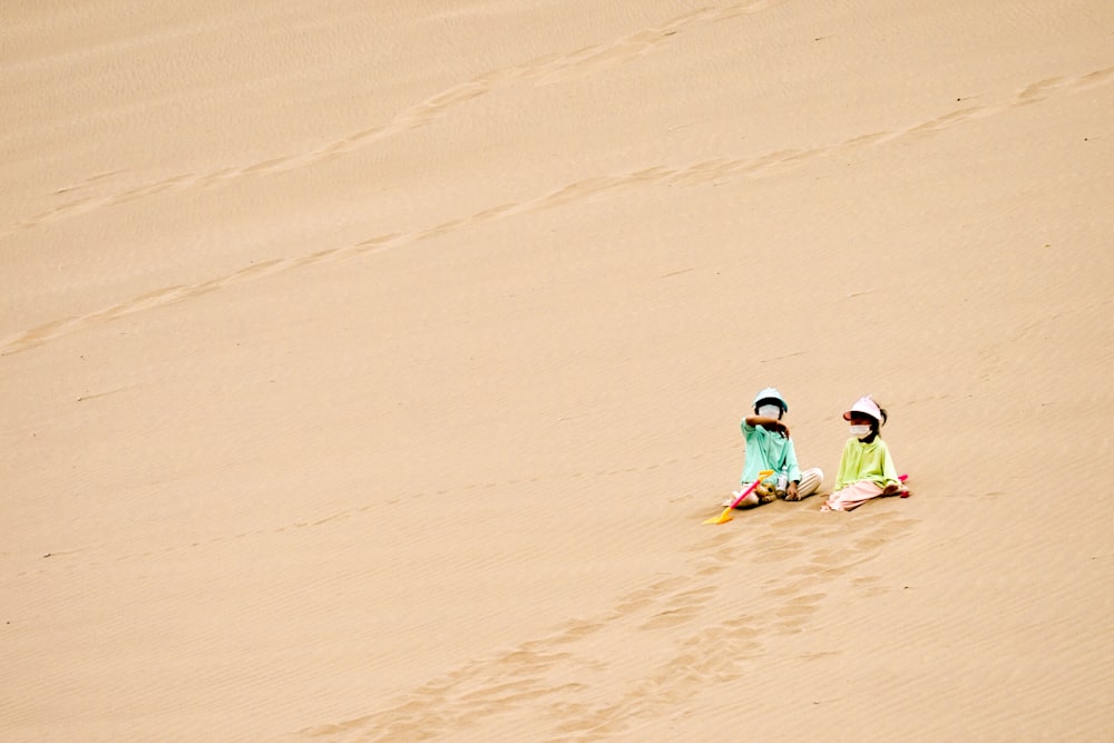 緑と黄色のウェットスーツを着た2人の子供が昼間、茶色の砂の上を歩く