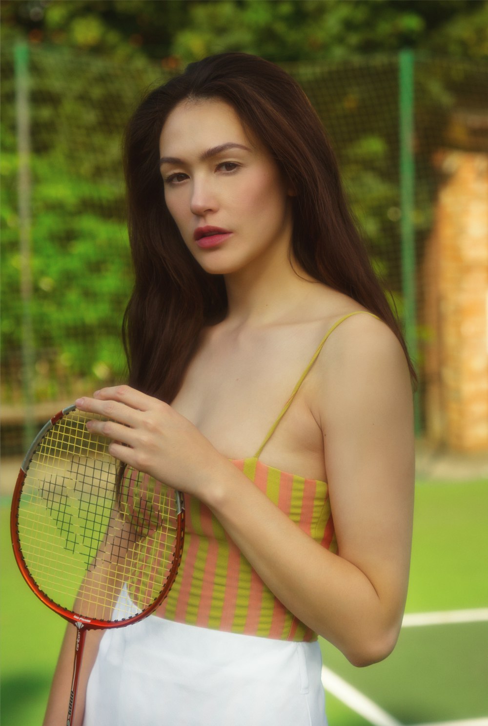 Mujer en la parte superior del bikini amarillo y verde sosteniendo la raqueta de tenis