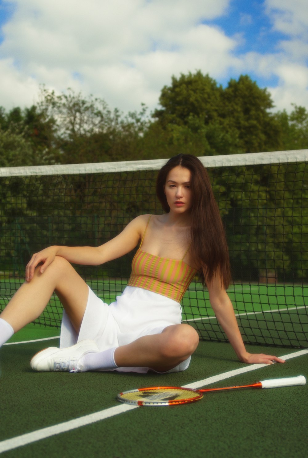 Frau im weißen Rock sitzt auf Tennisnetz