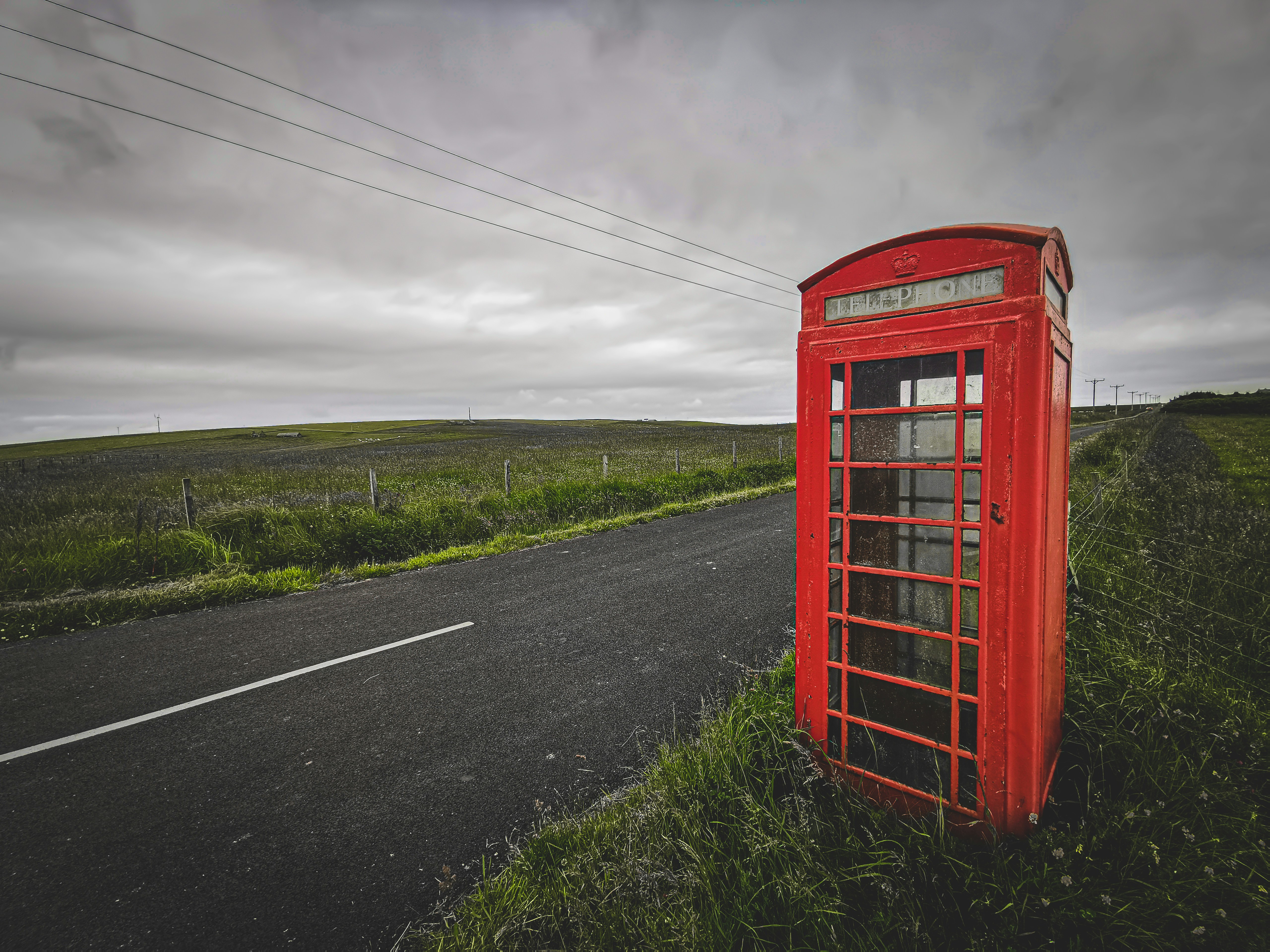 Cabina telefonica rossa sulla strada sotto il cielo nuvoloso durante il giorno