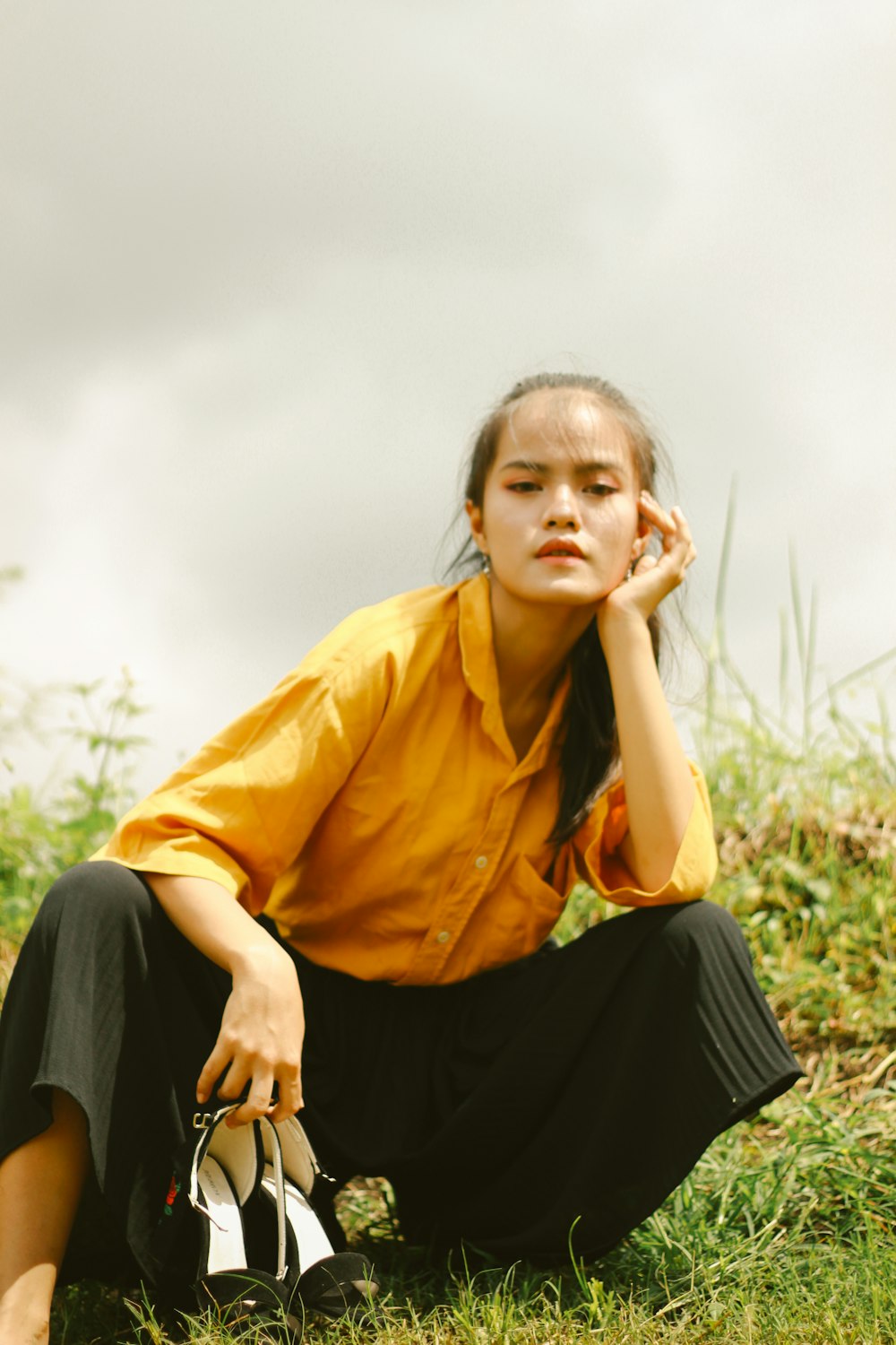 woman in yellow dress shirt and black skirt sitting on green grass during daytime