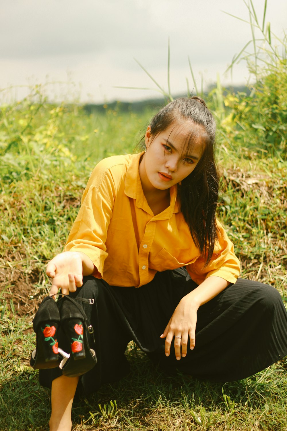 woman in yellow jacket and black pants sitting on green grass during daytime