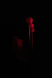 Three red spherical lamps are aligned vertically on poles, partially illuminating a dark background with hints of foliage.