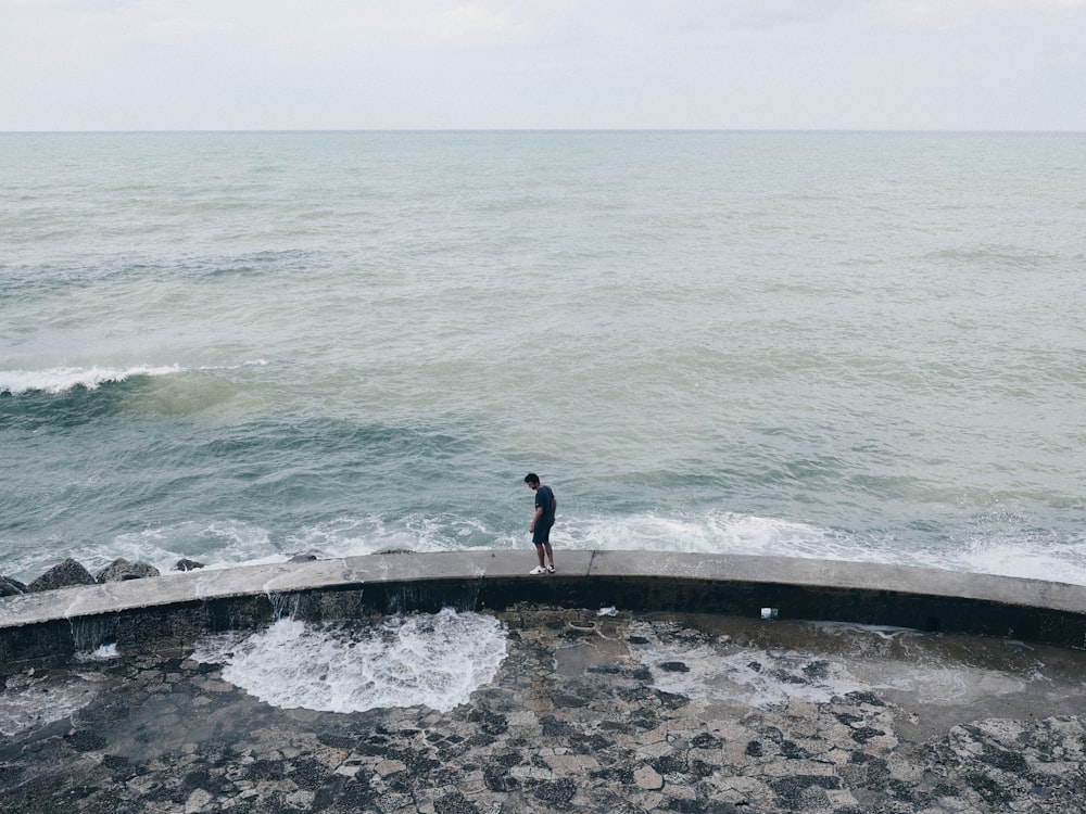 uomo in giacca nera in piedi sul marciapiede di cemento grigio vicino allo specchio d'acqua durante il giorno