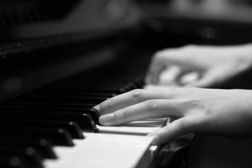 Hands are playing the keys of a piano, with fingers gracefully positioned over the black and white keys. The focus is on the movement and posture of the hands, suggesting a sense of rhythm and melody.