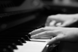Hands are playing the keys of a piano, with fingers gracefully positioned over the black and white keys. The focus is on the movement and posture of the hands, suggesting a sense of rhythm and melody.