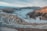 Terraced layers of an open-pit mine stretch across the rugged terrain, with swirling clouds nestled between the steep mountain ranges that frame the horizon. The rugged surface is marked by the distinct lines and curves of mining operations, contrasting with the smooth, ethereal mist that blankets the landscape, creating a dramatic interplay between industry and nature.