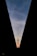 A silhouette of a communication tower is framed between two converging dark structures, set against a backdrop of a blue sky with soft, wispy clouds and a warm glow near the horizon.