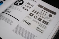 An open book spread displays a design layout featuring various grid patterns and text related to Rotterdam 2001. The layout includes different sizes and arrangements of squares and circles. There is prominent use of typography with words like 'Font', 'Rotterdam', and 'Europa' visible. The page contains both graphical elements and body text.