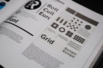 An open book spread displays a design layout featuring various grid patterns and text related to Rotterdam 2001. The layout includes different sizes and arrangements of squares and circles. There is prominent use of typography with words like 'Font', 'Rotterdam', and 'Europa' visible. The page contains both graphical elements and body text.