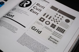 An open book spread displays a design layout featuring various grid patterns and text related to Rotterdam 2001. The layout includes different sizes and arrangements of squares and circles. There is prominent use of typography with words like 'Font', 'Rotterdam', and 'Europa' visible. The page contains both graphical elements and body text.