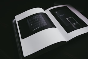An open book displaying two dark, abstract images on its pages. The lighting is dim, emphasizing the minimalistic and modern design of the inside pages. The images feature geometric patterns and minimal text.