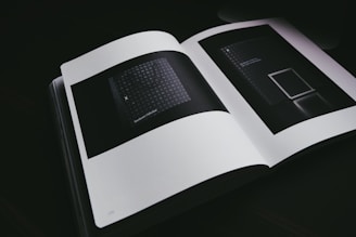 An open book displaying two dark, abstract images on its pages. The lighting is dim, emphasizing the minimalistic and modern design of the inside pages. The images feature geometric patterns and minimal text.