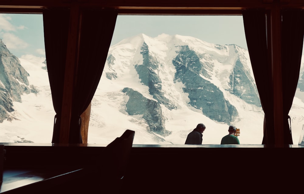 pessoa em pé perto de cerca de madeira marrom olhando para a montanha coberta de neve durante o dia