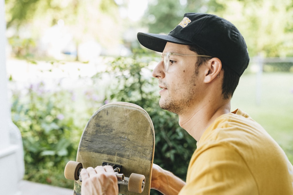 man in yellow shirt wearing black cap holding brown wooden guitar