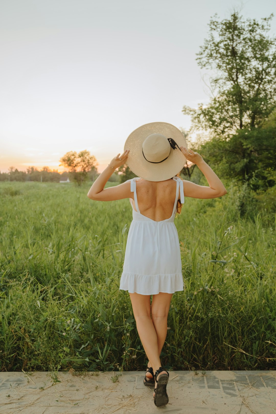 woman in white dress standing on green grass field during sunset