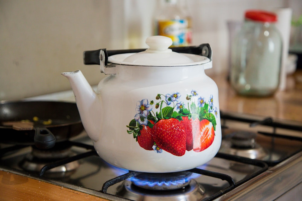 white and red strawberry print ceramic teapot on stove