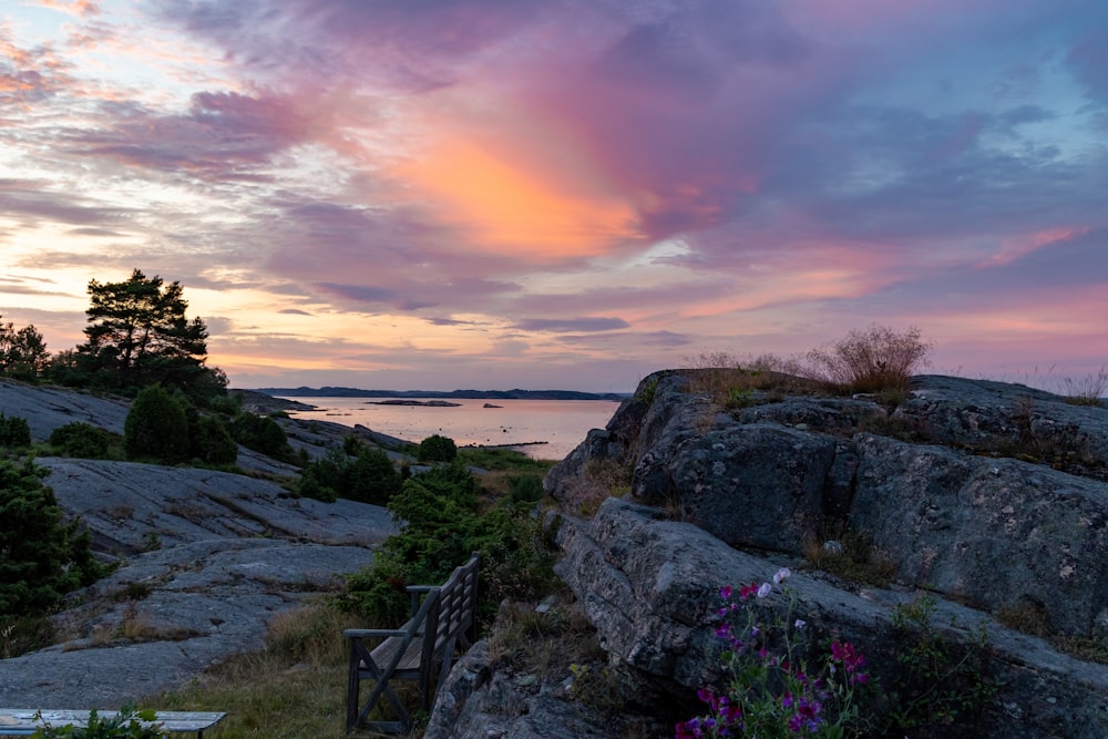 brown wooden table and chairs on gray rock formation near body of water during sunset