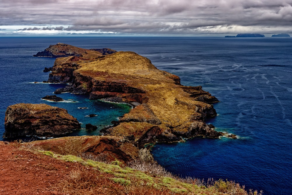 brown and green rock formation beside blue sea under white clouds during daytime