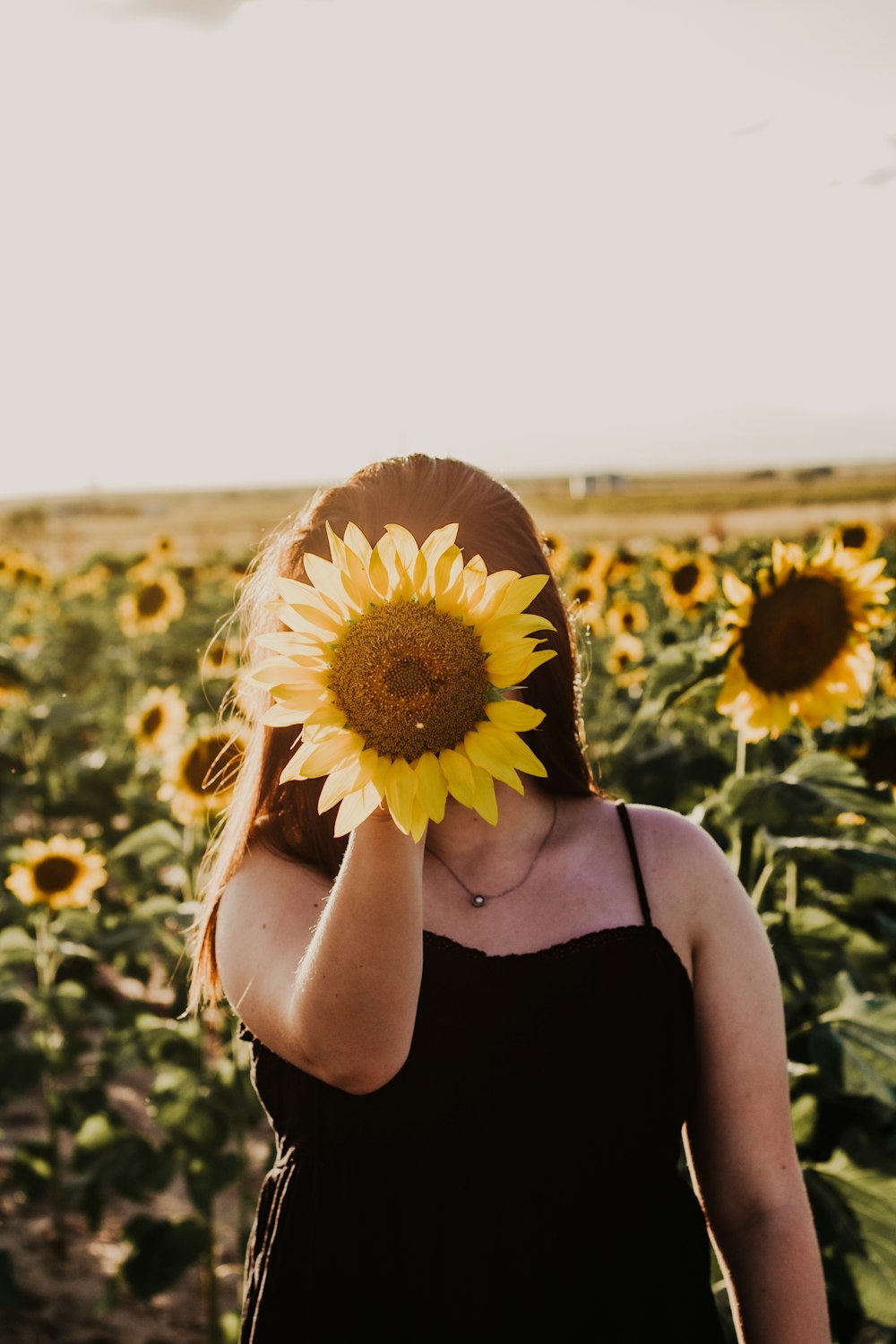 woman in black tank top holding sunflower during daytime