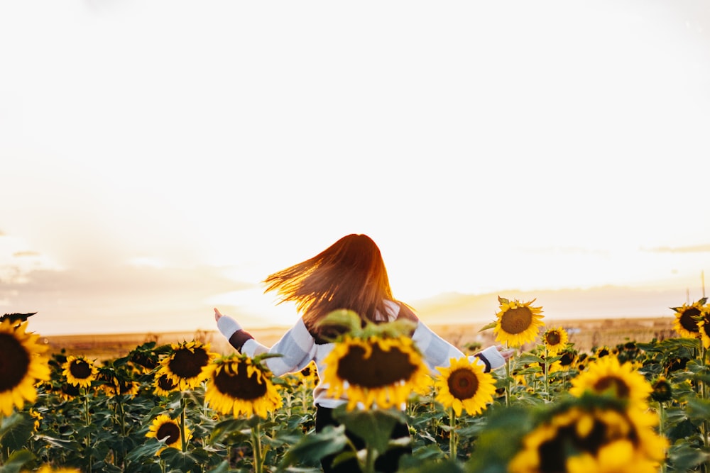 woman in white long sleeve shirt standing on sunflower field during daytime