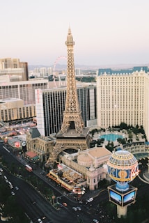 An urban landscape featuring a detailed replica of the Eiffel Tower surrounded by high-rise buildings, bustling streets, and a distinctive blue and golden globe structure. The scene captures the essence of a vibrant city with numerous hotels and casinos, indicative of a popular tourist destination.